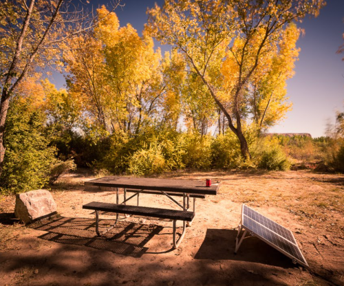 A picnic table under colorful autumn trees, with a solar panel nearby on a sunny day.